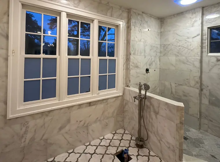 Freestanding tub suite wrapped in carrara marble tile at dusk